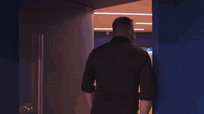 A Man In A Black Shirt Is Walking Through A Doorway GIF