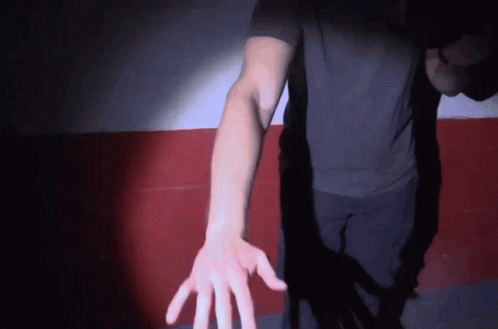A Man In A Black Shirt Reaches Out His Hand Towards The Camera GIF