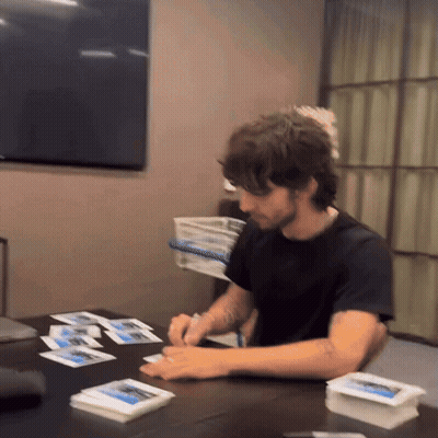 A Man In A Black Shirt Sits At A Table With A Bunch Of Cards On It GIF