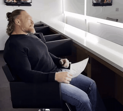 A Man In A Black Shirt Sits In A Chair GIF