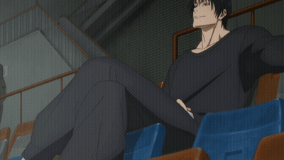 A Man In A Black Shirt Sits In A Stadium With His Legs Crossed GIF