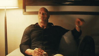 A Man In A Black Shirt Sits On A Couch Holding A Glass Of Whiskey GIF