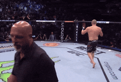 A Man In A Black Shirt Stands In A Boxing Ring With The Word Ufc On The Ground GIF