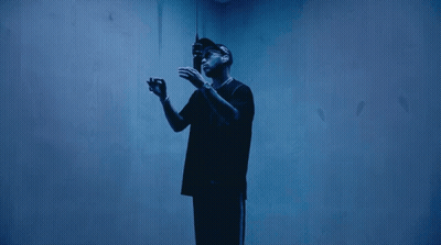 A Man In A Black Shirt Stands In A Dark Room GIF