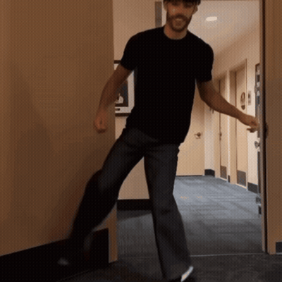 A Man In A Black Shirt Stands In A Hallway GIF