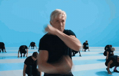 A Man In A Black Shirt Stands In Front Of A Group Of People GIF