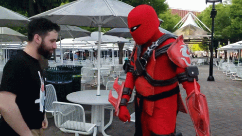A Man In A Black Shirt Stands In Front Of A Red Costume GIF