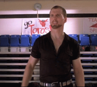 A Man In A Black Shirt Stands In Front Of A Sign That Says Go Toros GIF