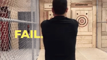 A Man In A Black Shirt Stands In Front Of A Wooden Target That Says Fail On It GIF