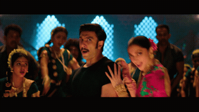 A Man In A Black Shirt Stands Next To A Woman In A Pink And Green Dress GIF