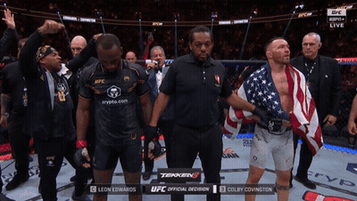 A Man In A Black Shirt That Says Ufc Stands Next To A Man In An American Flag GIF