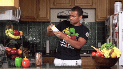 A Man In A Black Shirt That Says Vegetables Is Standing In The Kitchen GIF