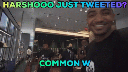 A Man In A Black Shirt With A Skull On It Stands In Front Of A Sign That Says Harshooo GIF