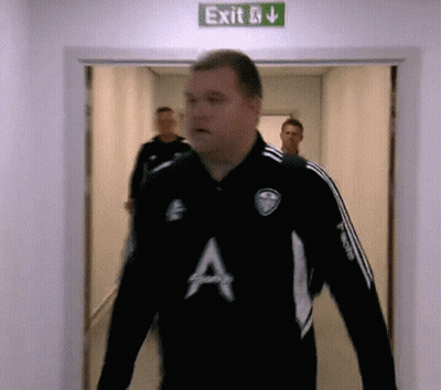 A Man In A Black Shirt With The Letter A On It Walks Through An Exit Sign GIF
