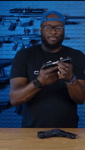 A Man In A Black Shirt With The Letter C On The Front Is Holding A Gun GIF