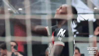 A Man In A Black Shirt With The Letter K On It Is Behind A Fence GIF