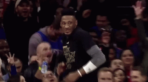 A Man In A Black Shirt With The Word Victory On It Is Standing In Front Of A Crowd Of People . GIF