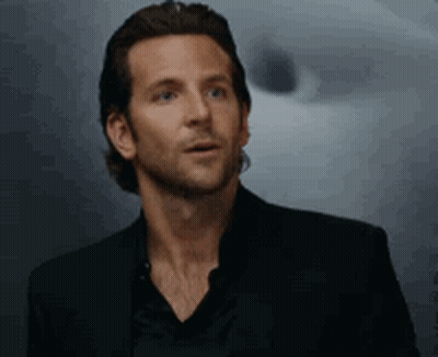 A Man In A Black Suit And Black Shirt Is Standing In Front Of A Wall . GIF