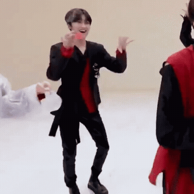 A Man In A Black Suit And Red Shirt Is Dancing On A White Floor While Holding A Donut . GIF