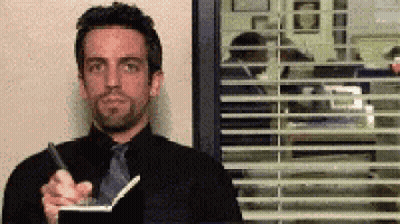 A Man In A Black Suit And Tie Is Holding A Pen And A Notebook GIF