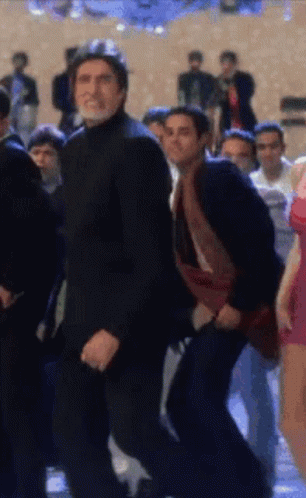 A Man In A Black Suit Is Dancing In A Crowd Of People GIF