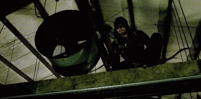 A Man In A Black Suit Is Holding A Bow And Arrow While Sitting On A Ledge . GIF