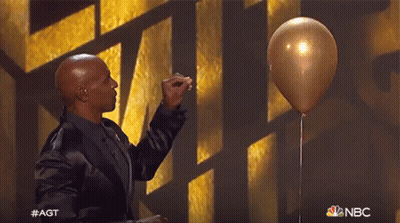 A Man In A Black Suit Is Holding A Gold Balloon In Front Of A Nbc Logo GIF