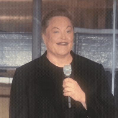 A Man In A Black Suit Is Holding A Microphone And Making A Funny Face GIF
