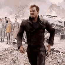 A Man In A Black Suit Is Running In Front Of A Group Of People In A Field . GIF