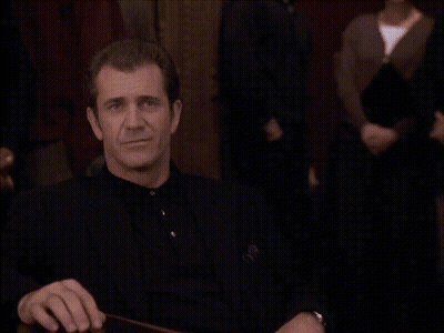 A Man In A Black Suit Is Sitting At A Table Making A Funny Face GIF