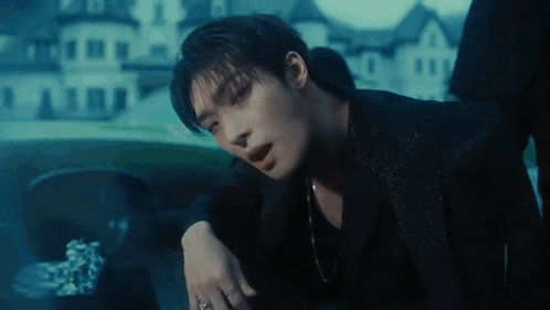 A Man In A Black Suit Is Sitting In A Car With His Hand On His Shoulder . GIF
