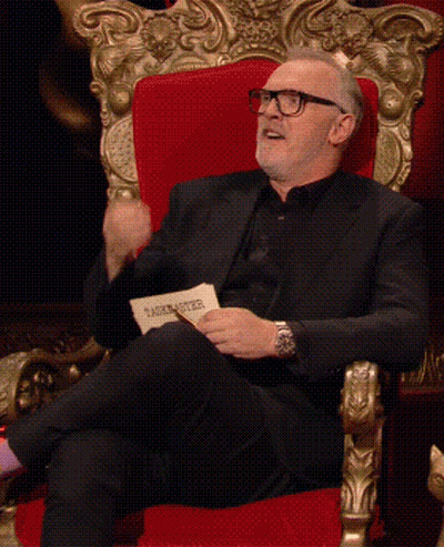 A Man In A Black Suit Is Sitting In A Red Chair GIF