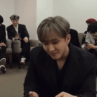 A Man In A Black Suit Is Sitting In A Room With Other Men GIF