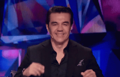 A Man In A Black Suit Is Smiling In Front Of A Blue Background GIF