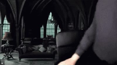 A Man In A Black Suit Is Standing In A Dark Room . GIF