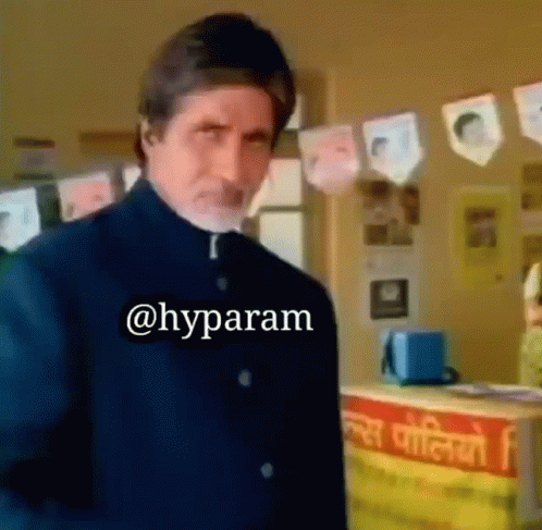 A Man In A Black Suit Is Standing In Front Of A Counter With A Sign That Says ' @Hyparam ' On It GIF