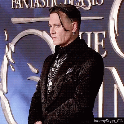 A Man In A Black Suit Is Standing In Front Of A Fantastic Beasts Sign GIF