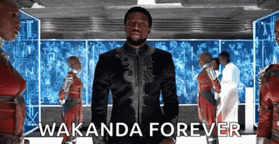A Man In A Black Suit Is Standing In Front Of A Group Of People With The Words Wakanda Forever . GIF