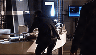 A Man In A Black Suit Is Standing In Front Of A Monitor GIF