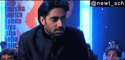 A Man In A Black Suit Is Standing In Front Of A Sign That Says Riya GIF