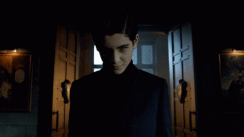 A Man In A Black Suit Stands In A Dark Hallway GIF