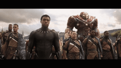A Man In A Black Suit Stands In A Line With Other Men GIF