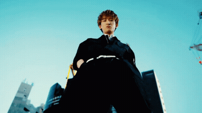 A Man In A Black Suit Stands In Front Of A Building That Says ' Tokyo ' On It GIF