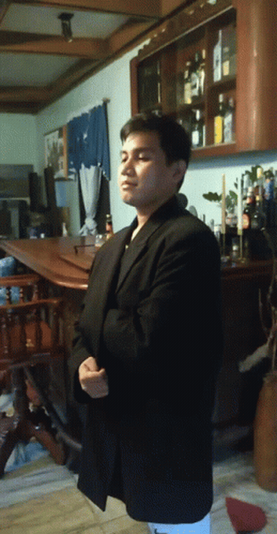 A Man In A Black Suit Stands In Front Of A Shelf Full Of Bottles GIF