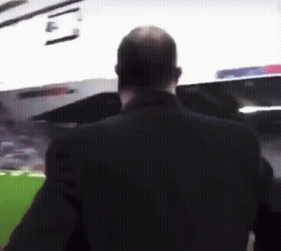A Man In A Black Suit Stands In Front Of A Stadium GIF