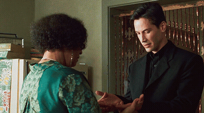 A Man In A Black Suit Stands Next To A Woman In A Green Dress GIF