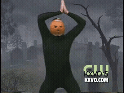 A Man In A Black Suit With A Pumpkin On His Head Is Dancing In A Cemetery . GIF