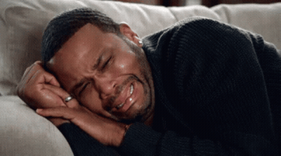 A Man In A Black Sweater Is Laying On A Couch Crying . GIF