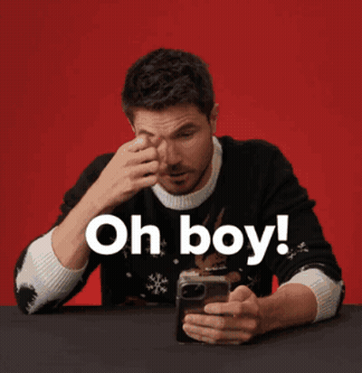 A Man In A Black Sweater Is Looking At His Phone And Says Oh Boy GIF