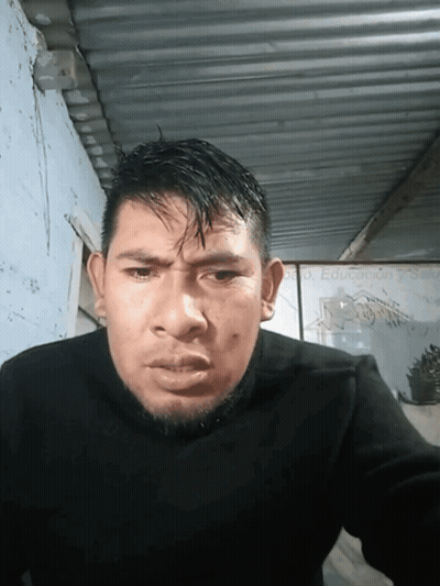 A Man In A Black Sweater Is Looking At The Camera With A Sign In The Background That Says Dr. Eduardo Garcia GIF